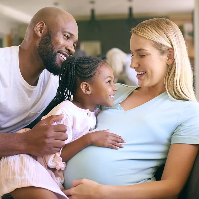Family With Daughter Cuddling Pregnant Mother At Home Together
